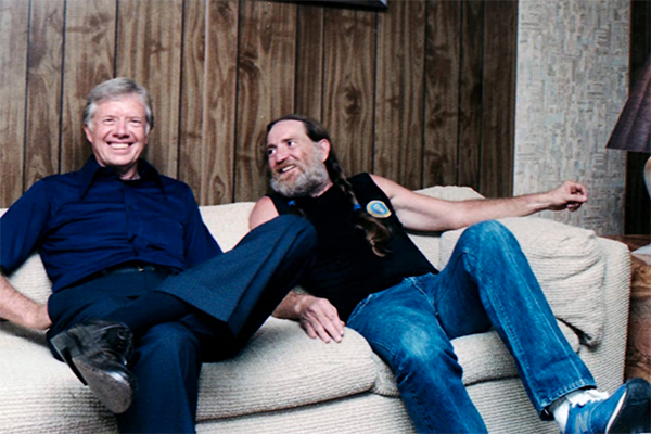 Willie Nelson and Jimmy Carter sit on a couch.